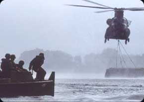 Bridge Crewmembers work closely with CH-47 Chinook helicopters as they prepare for a bridge section to be placed in the water.  These bridge sections are also known as bread loafs.