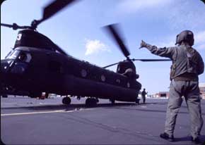 A CH-47 Crew Chief communicates to the pilots from the tarmac during a pre-flight spin-up.